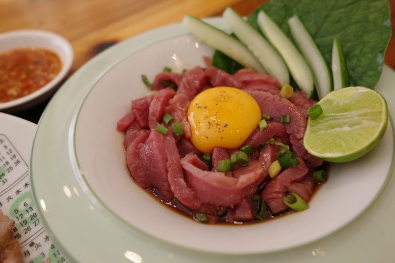 เนื้อดิบหั่นเส้นราดน้ำปรุง โปะไข่แดง วางคู่มะนาวและแตงกวา
