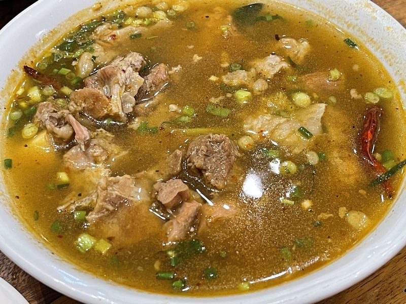 ต้มแซ่บน้ำใสในชามใหญ่ มีเนื้อเปื่อยและพริกแห้ง