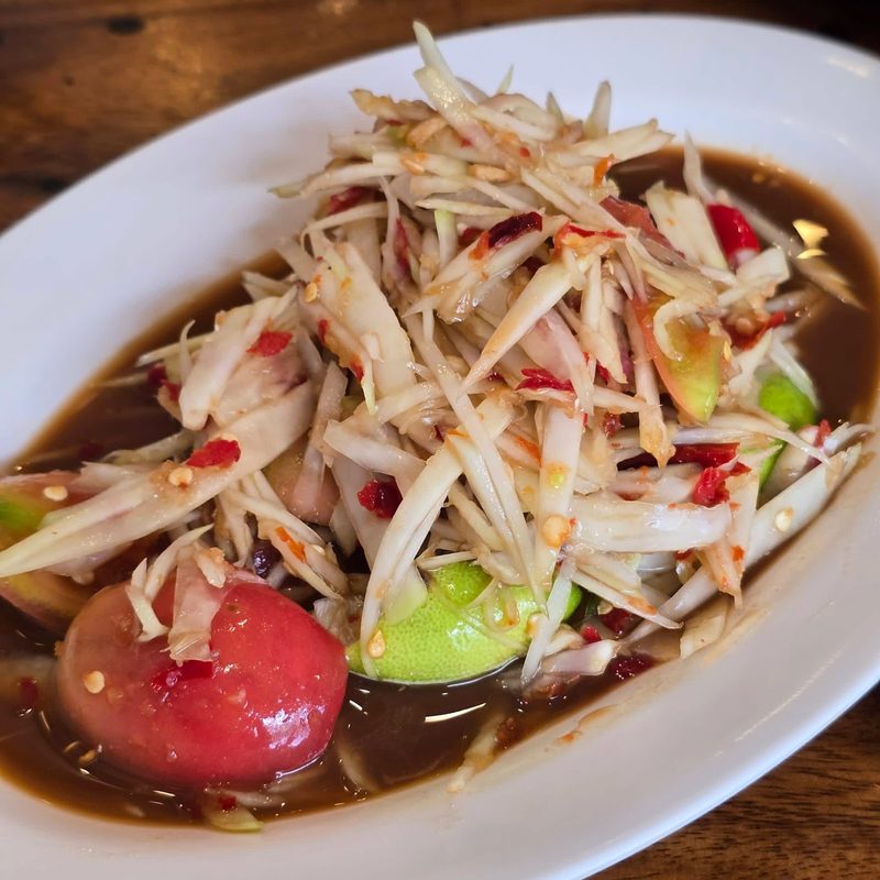 ส้มตำปลาร้าน้ำสีเข้ม ใส่มะเขือเทศและมะนาว