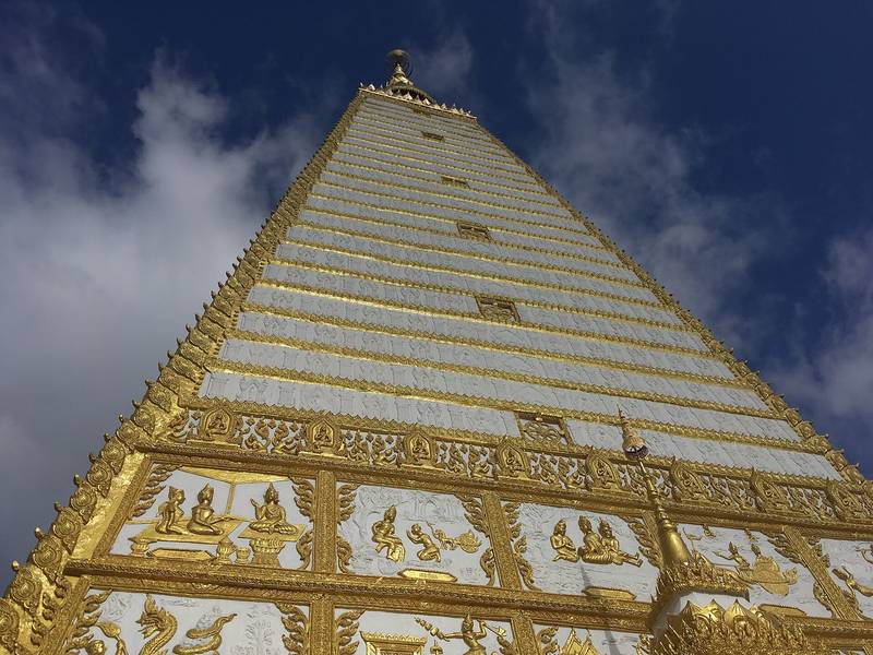 เจดีย์สีขาวขอบทองทรงสี่เหลี่ยมสูง มองจากด้านล่างตัดกับฟ้า